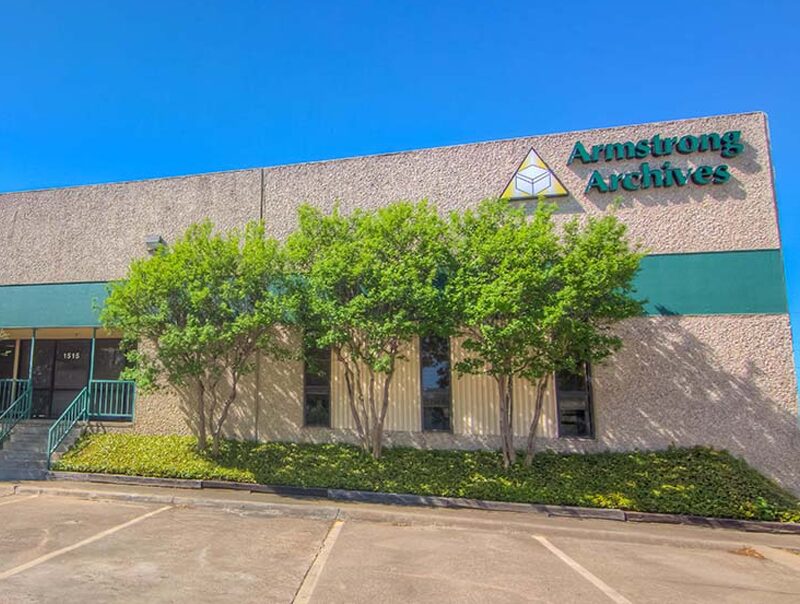 The Armstrong Archives business building standing under a clear blue sky, with a line of trees and a parking lot in front.